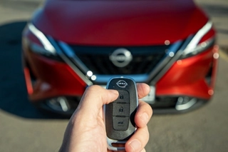 A hand holding a Nissan Key in front of Nissan car