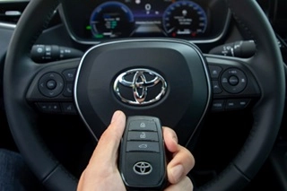 A hand holding a Toyota Key in front of Toyota steerinf wheel