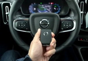 A hand holding a Volvo Key in front of Volvo steering wheel